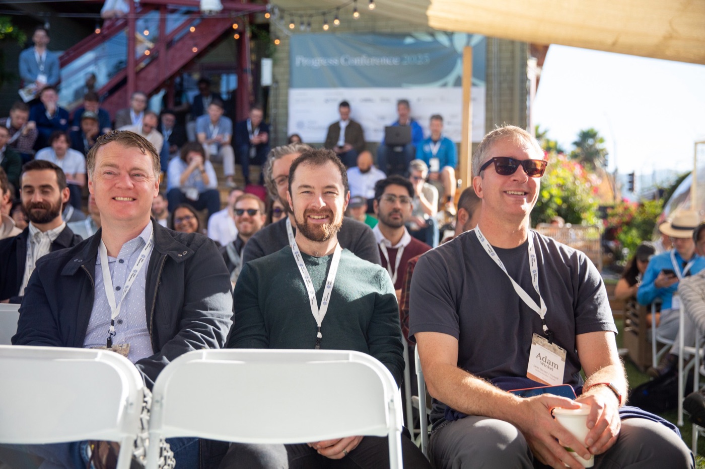 Smiling attendees seated in the front rows at an outdoor session of the Progress Conference.